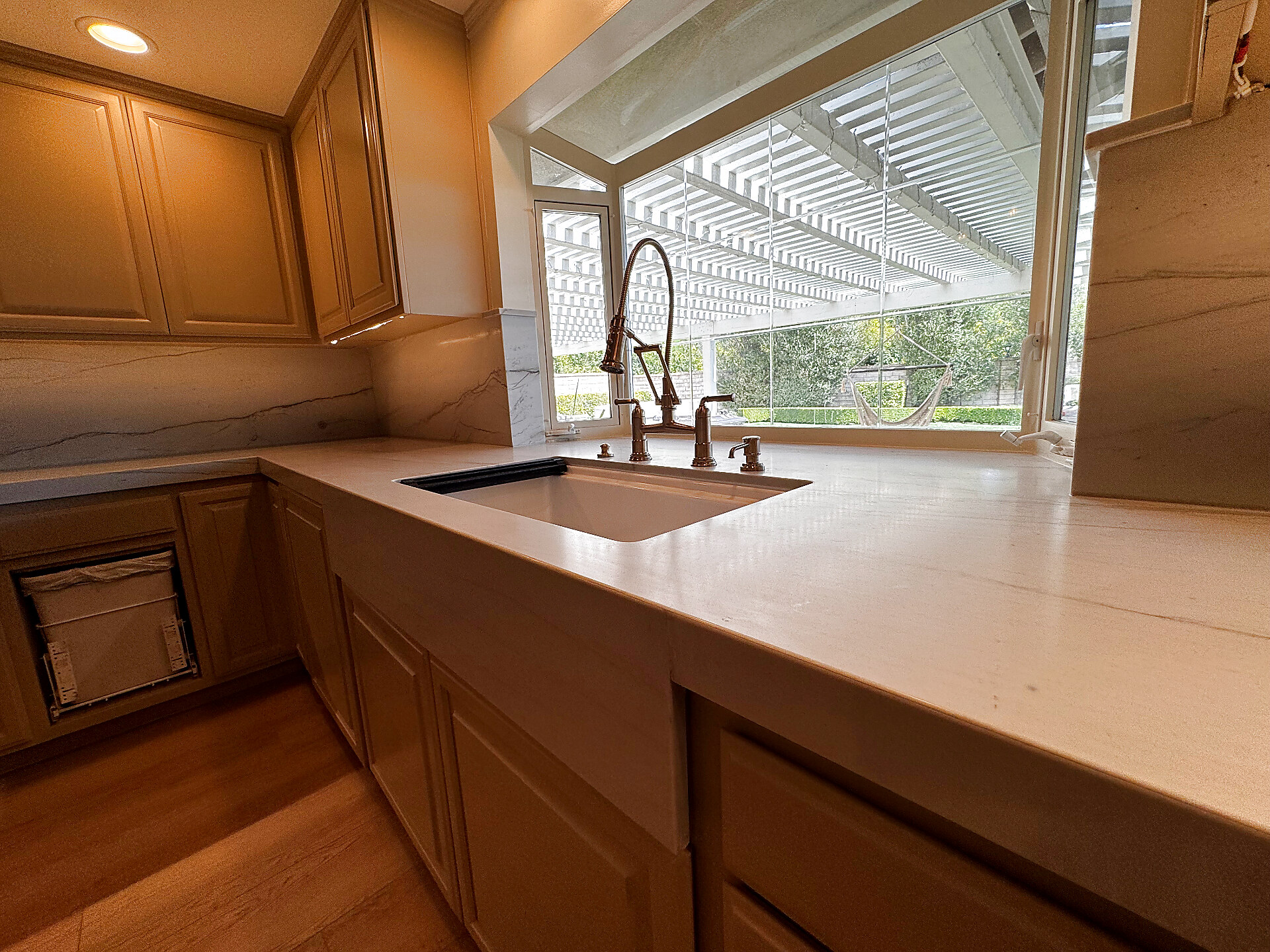 Waterfall-style white quartz sink run with backyard view and bronze faucet