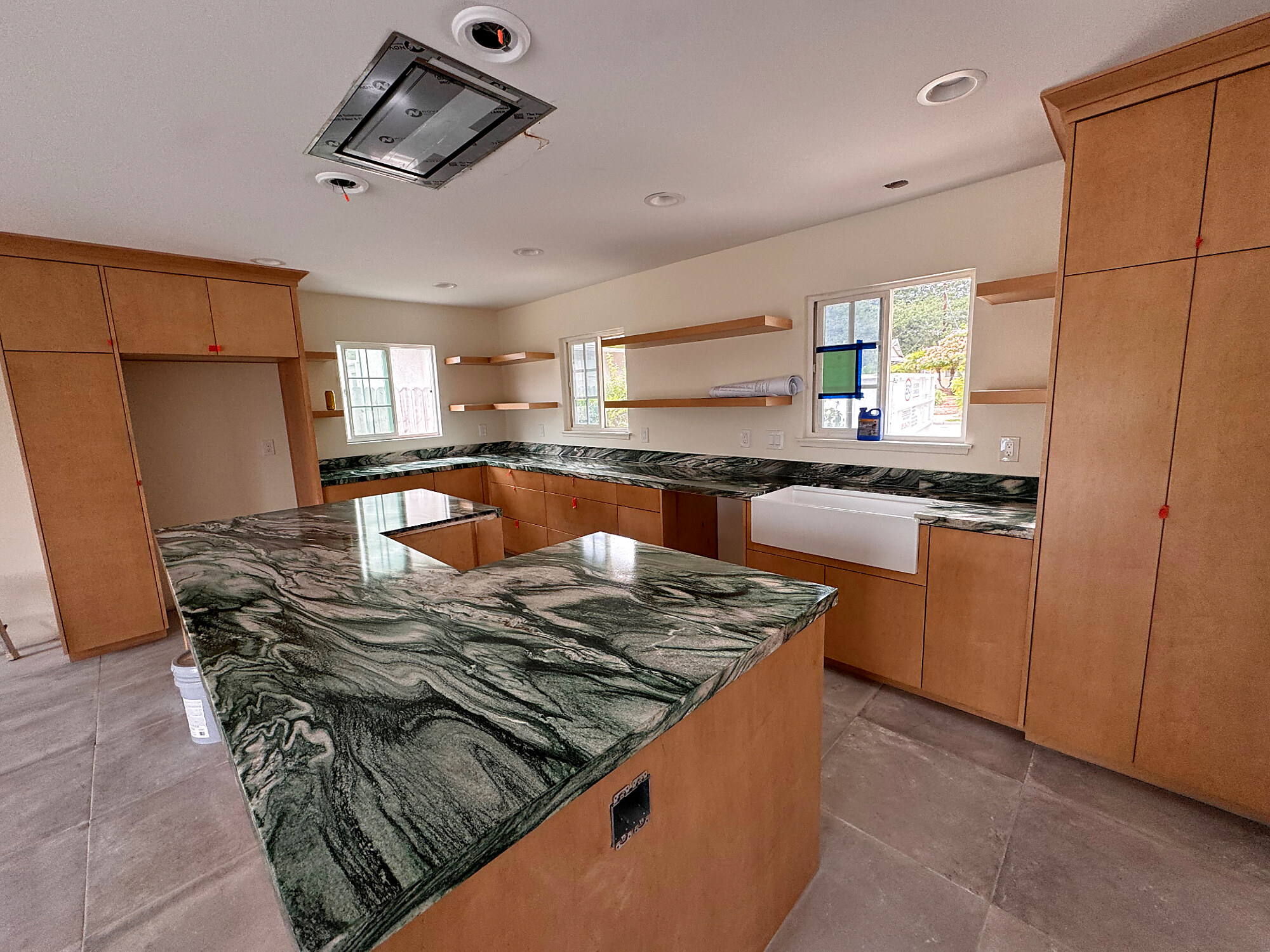 Dramatic green marble countertops with maple cabinetry and apron sink
